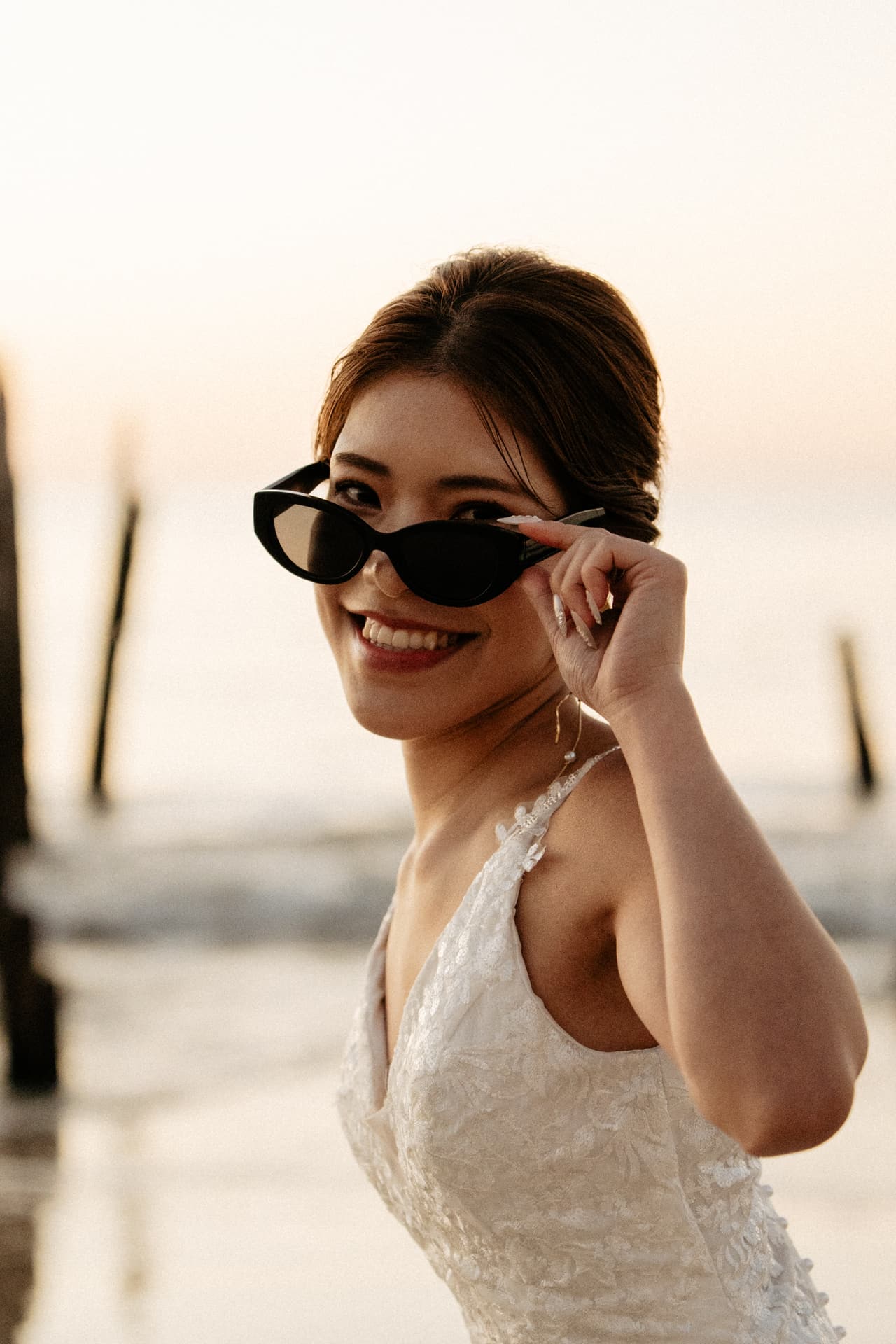Sayuri smiling as she lowers her sunglasses beside the jetty posts at dusk