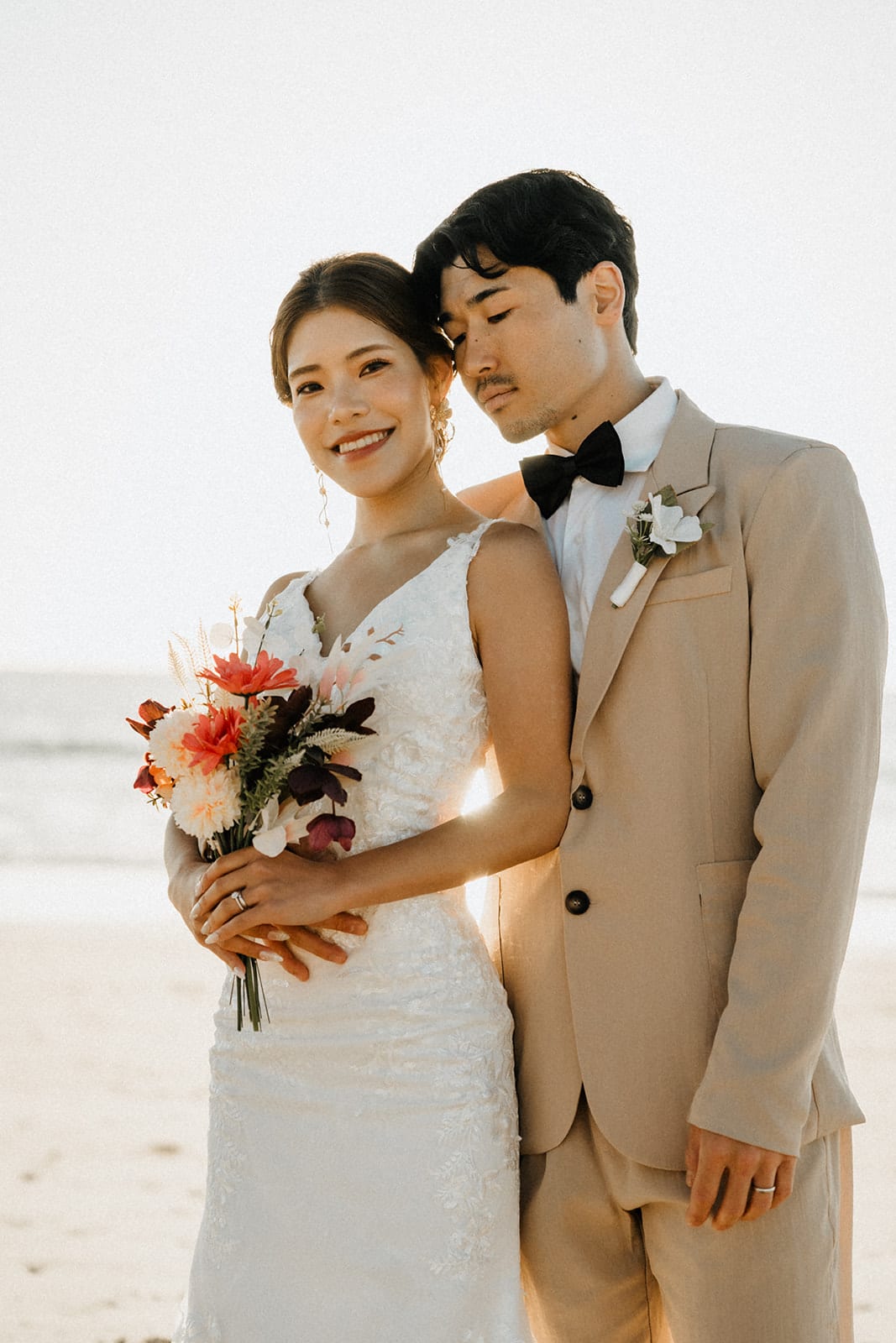 Sayuri smiling with her bouquet as Shuto leans his head towards hers on the bright beach