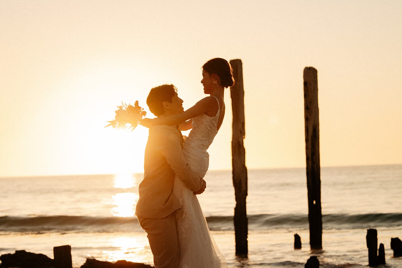Shuto lifting Sayuri beside the old jetty posts as the sun sets behind them