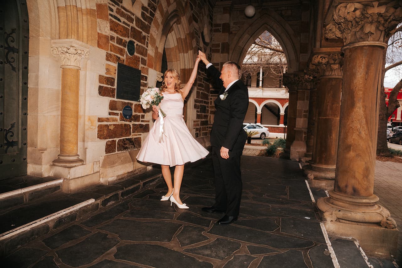 Jon twirling Terrie under sandstone Gothic arches