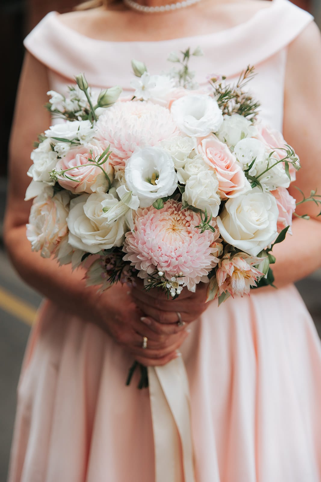 Close up of Terrie holding her bouquet of white and pale pink roses against her pink dress