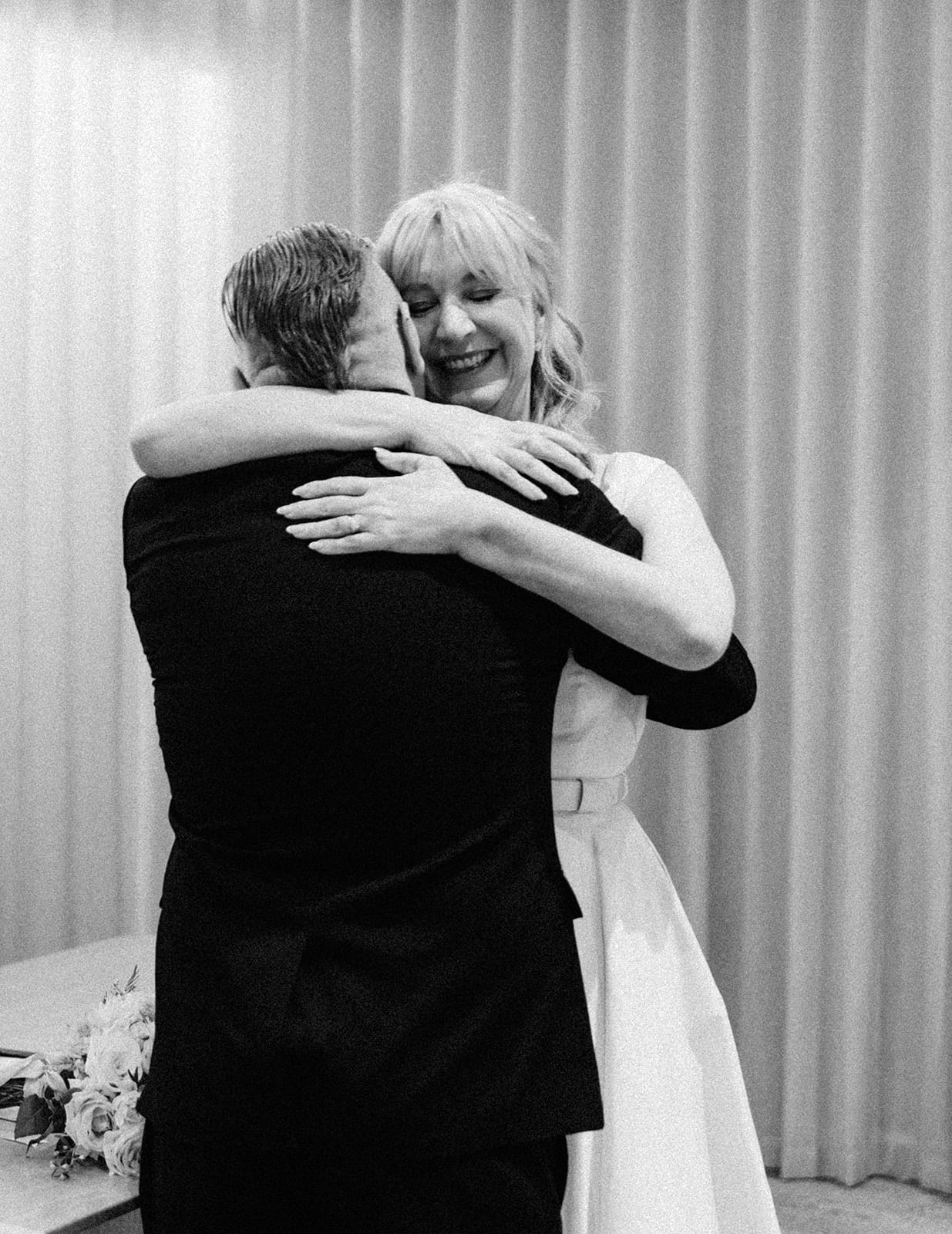 Black and white photo of Terrie laughing as she hugs Jon tight after the vows