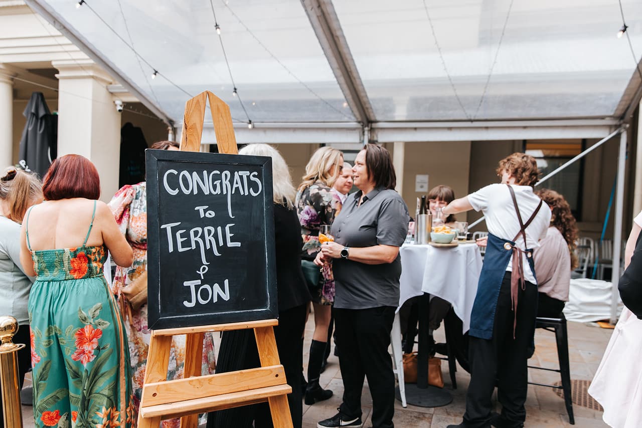 A chalkboard on an easel that reads Congrats to Terrie & Jon, among the guests under the marquee