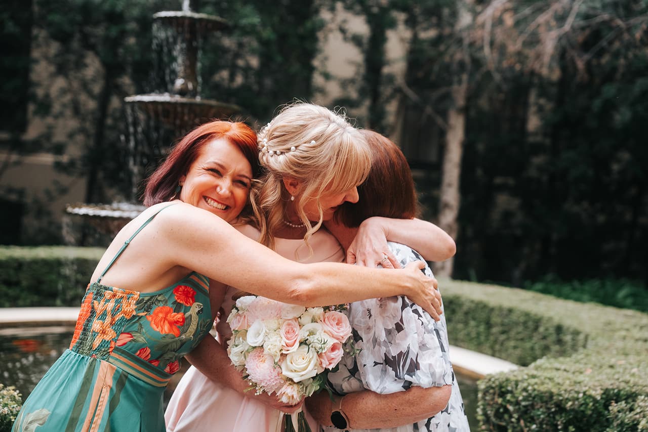 Terrie wrapped in a hug by two friends beside the fountain in the courtyard