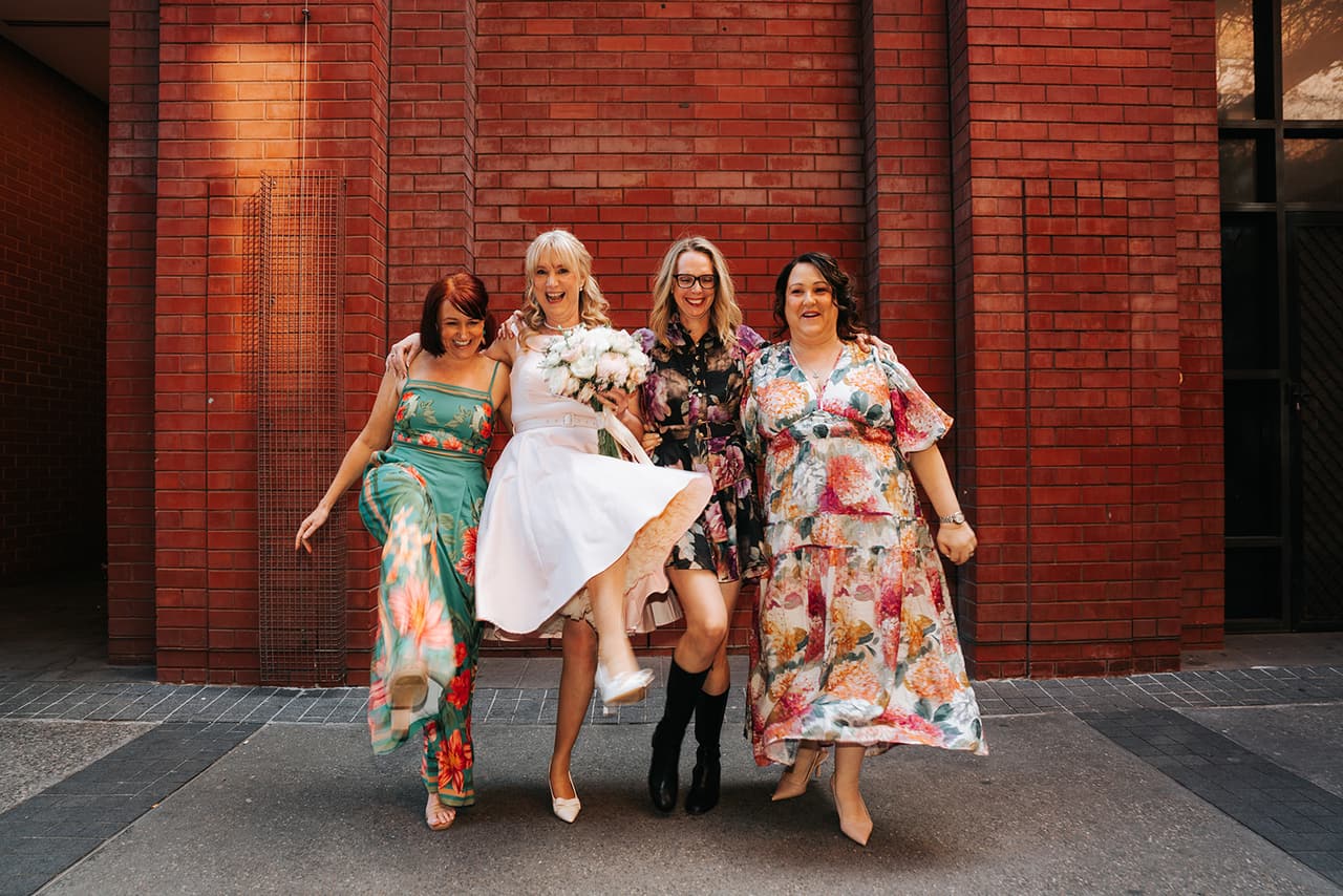 Terrie and her friends kicking up their heels in front of a red brick wall after the ceremony