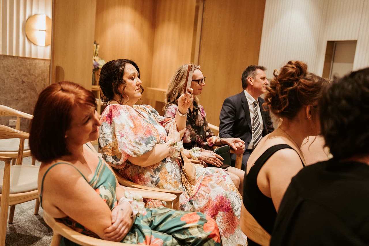 Guests in floral dresses smiling as they watch the ceremony from their seats