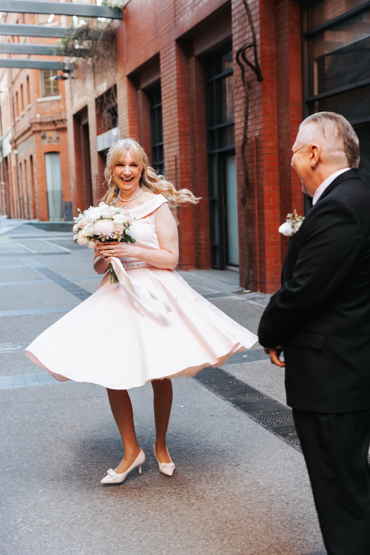 Terrie twirling her pink dress in the laneway outside the registry as Jon watches