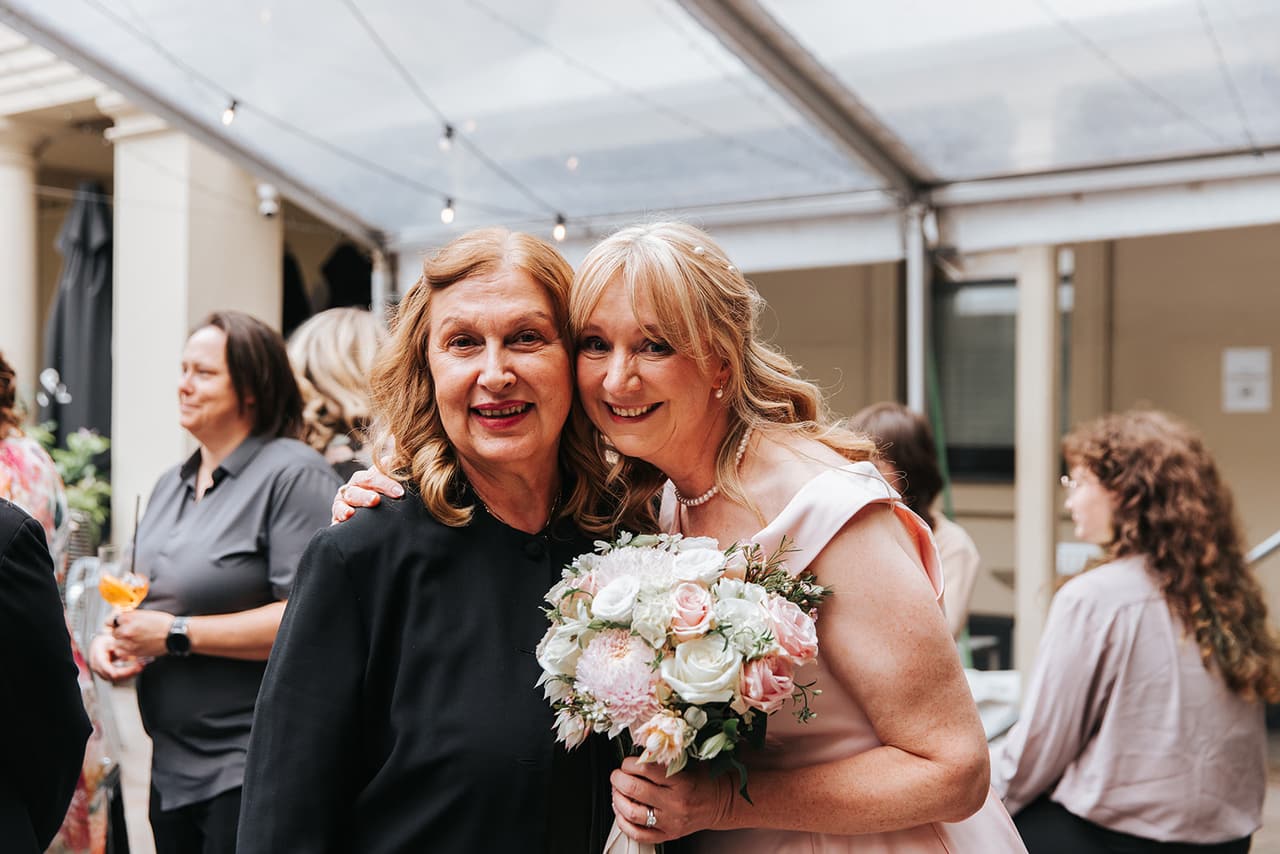 Terrie and a friend smiling cheek to cheek under the clear marquee in the courtyard