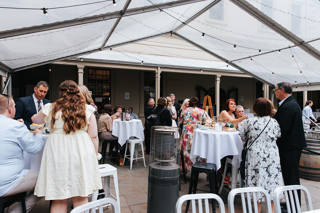 Guests mingling around high tables under the clear marquee in the courtyard
