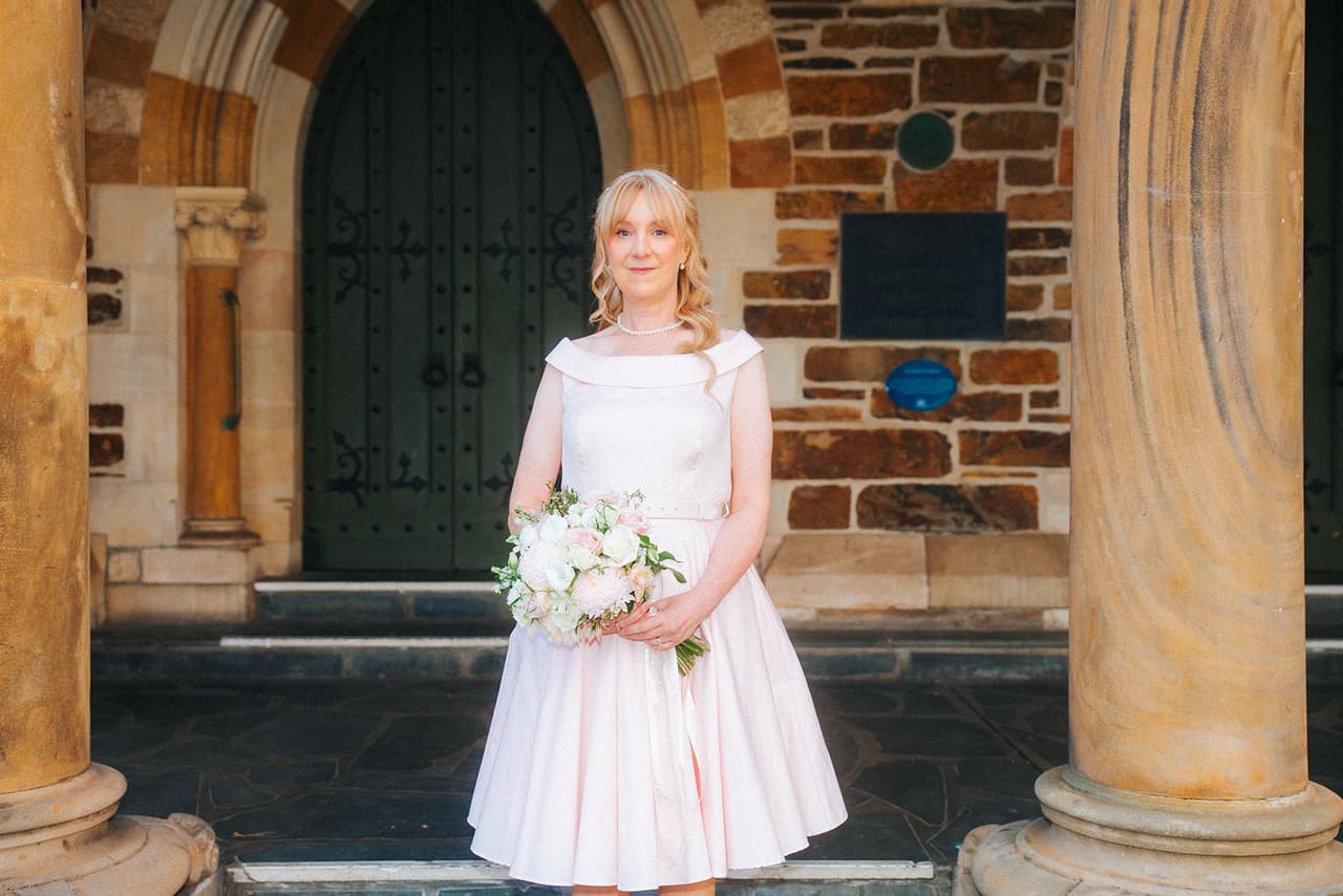 Terrie holding her bouquet between two sandstone columns, a heavy timber church door behind her