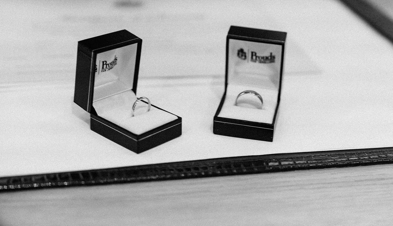 Black and white photo of two wedding rings in open ring boxes on the signing table