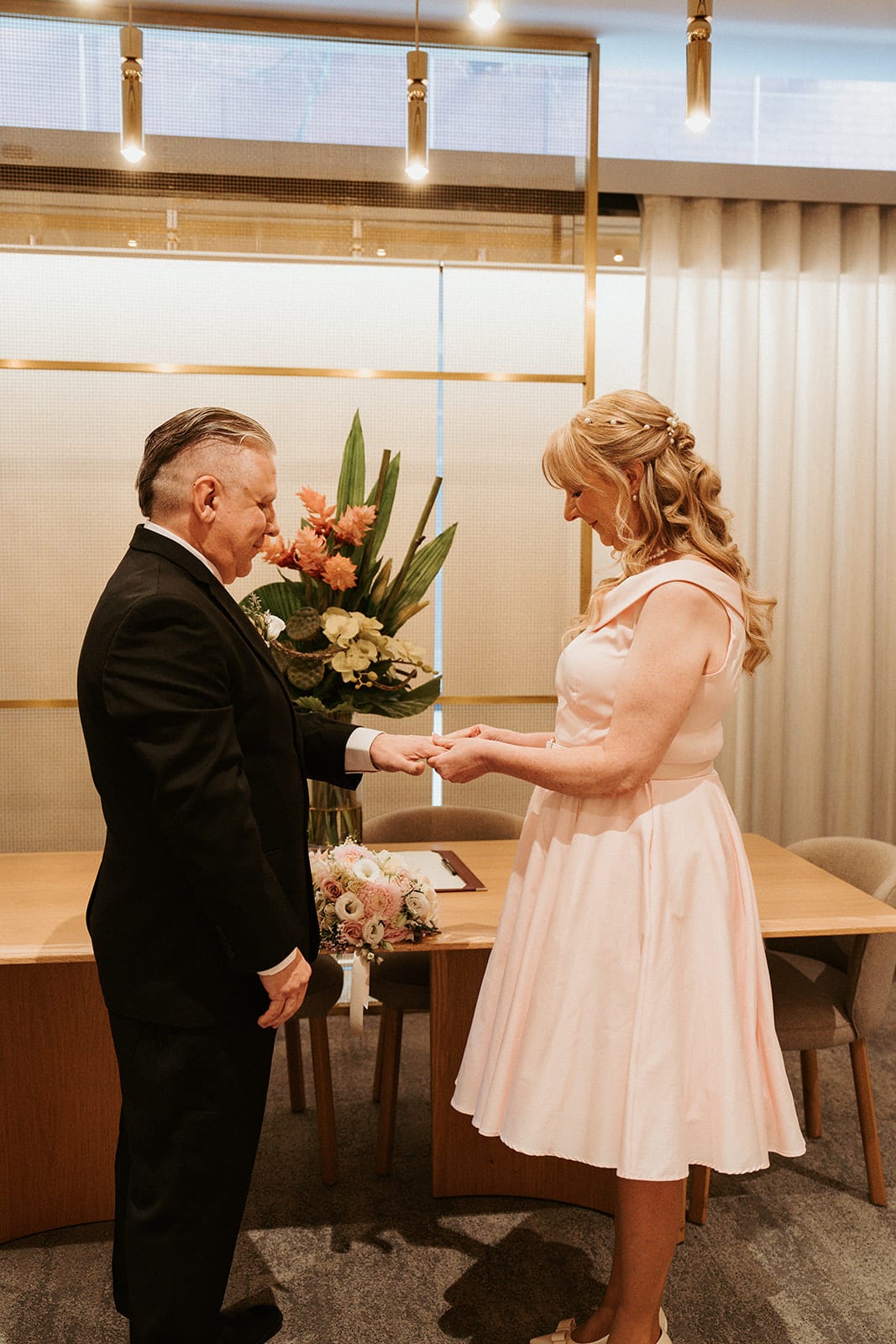 Jon and Terrie exchanging rings at the long table, a tall vase of flowers beside them